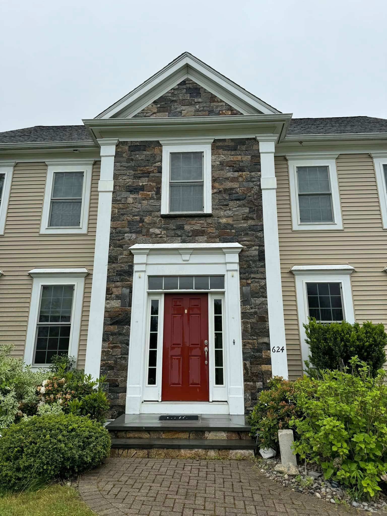 Front view of a gray house with stone columns and a red front door