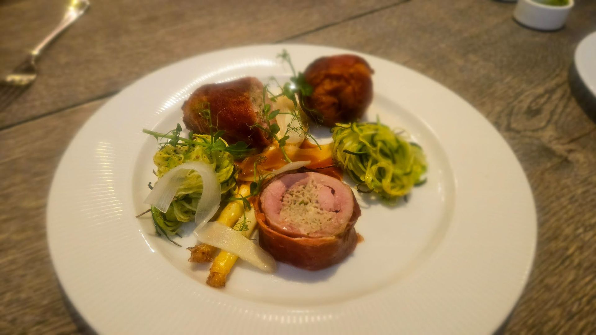 Tallerkeneret gourmetmåltid med skåret kød, grøntsager og sauce på et hvidt fad.