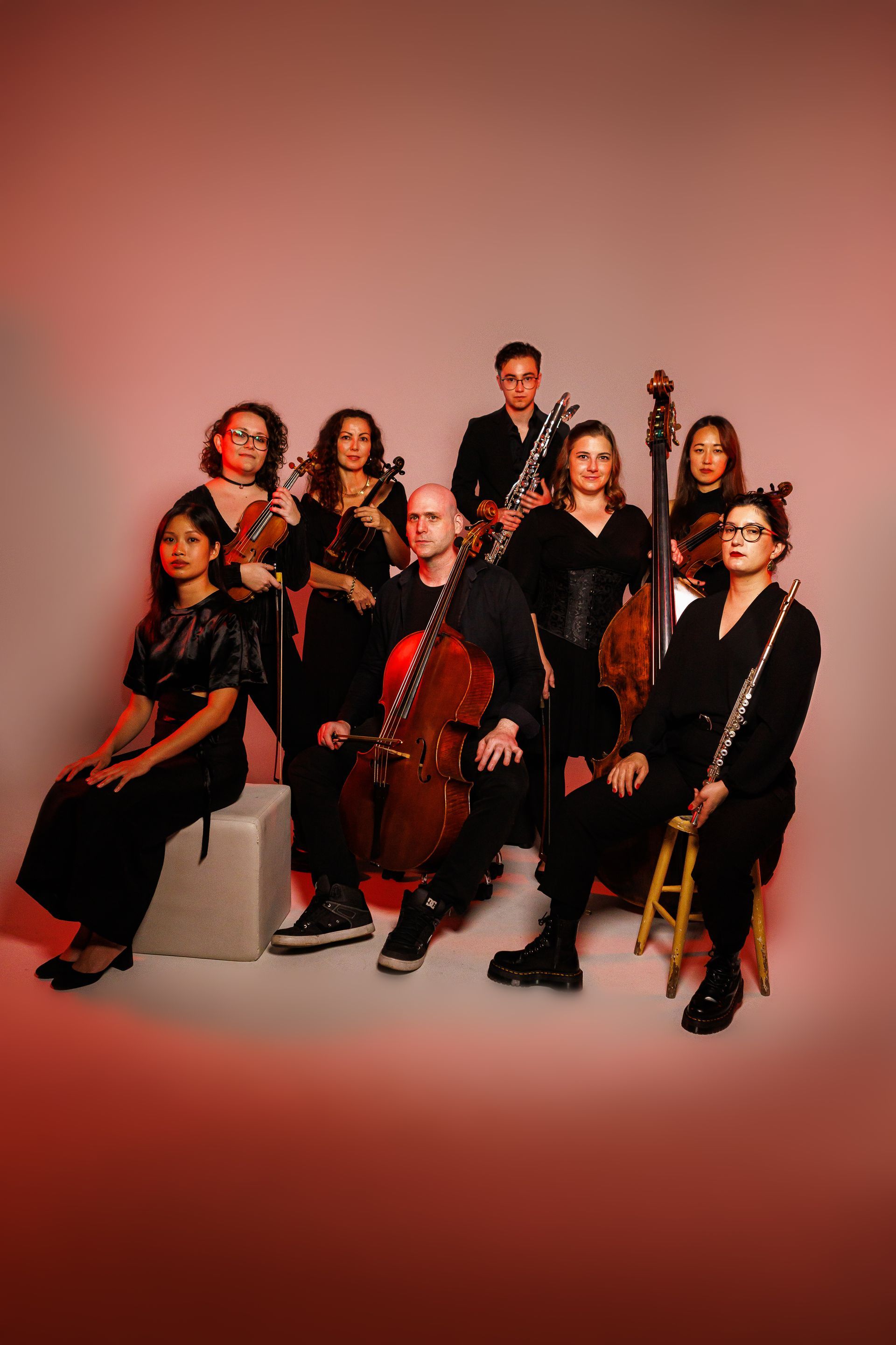 Brisbane Tango Orchestra - Seven musicians pose in a studio with string instruments against a pink-red backdrop.