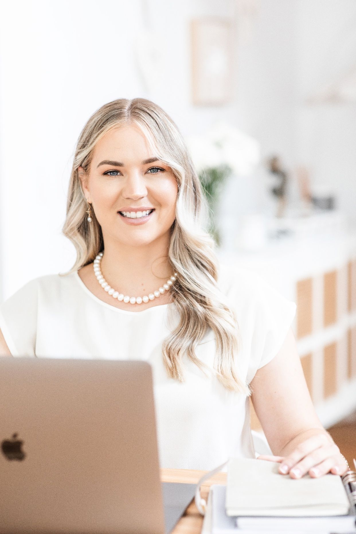 Pearl Class Communications - Smiling woman at a desk with a laptop and notebooks in a bright office