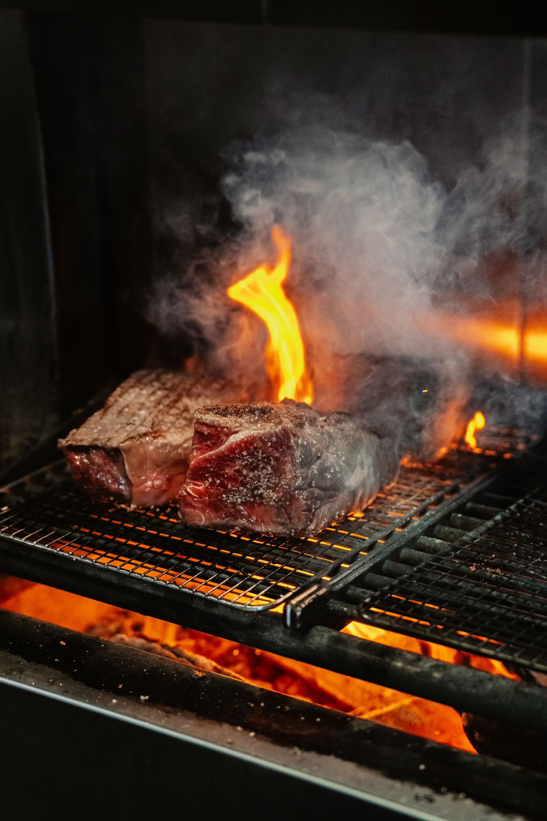 Char House Toowoomba - Steak grilling over open flames with smoke rising on a barbecue grate