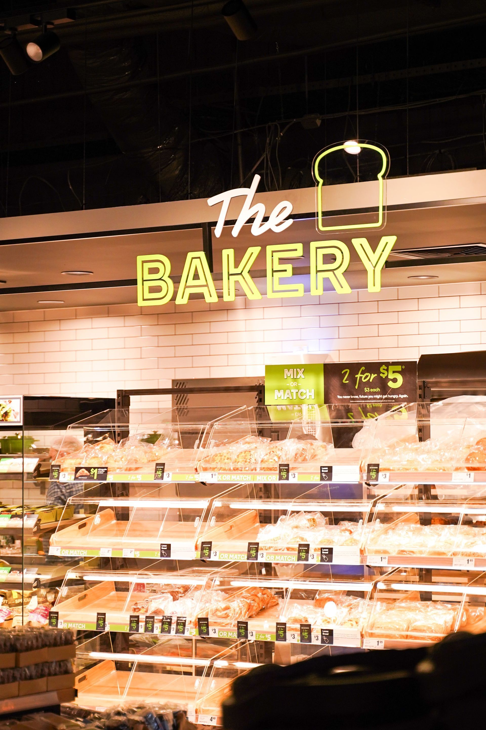 A bakery in a grocery store with a neon sign hanging from the ceiling.