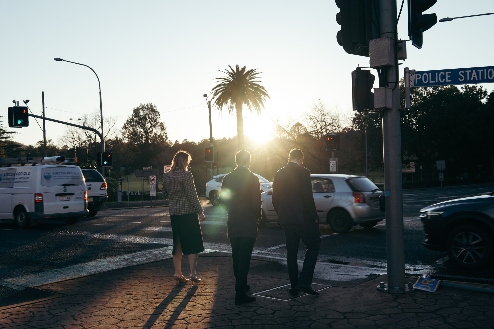MacDonald Law - Pedestrians crossing a street at sunset near a police station sign and traffic lights