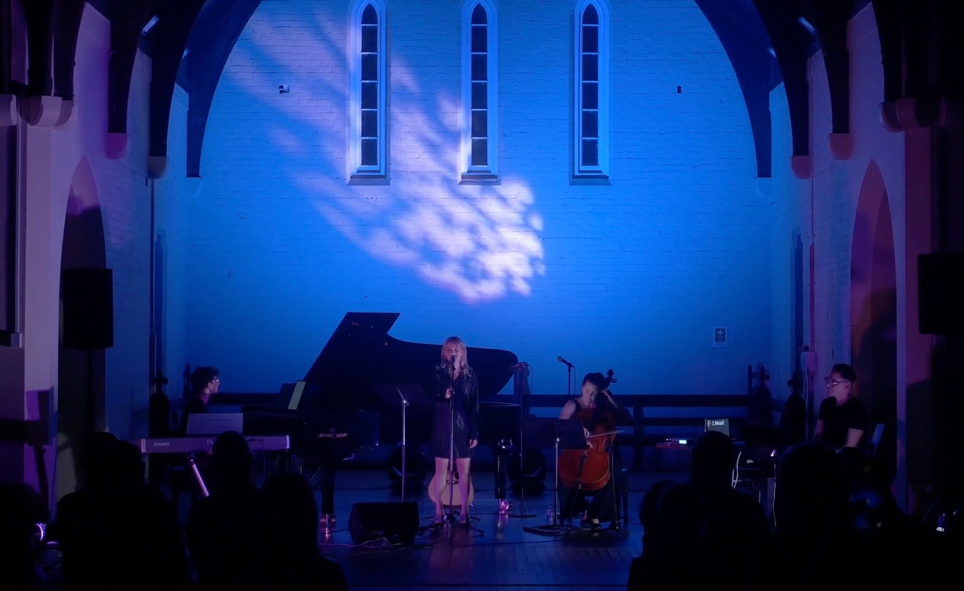 Brisbane Music Festival - Blue-lit stage with musicians performing in a church-like hall, with a piano and drums visible.