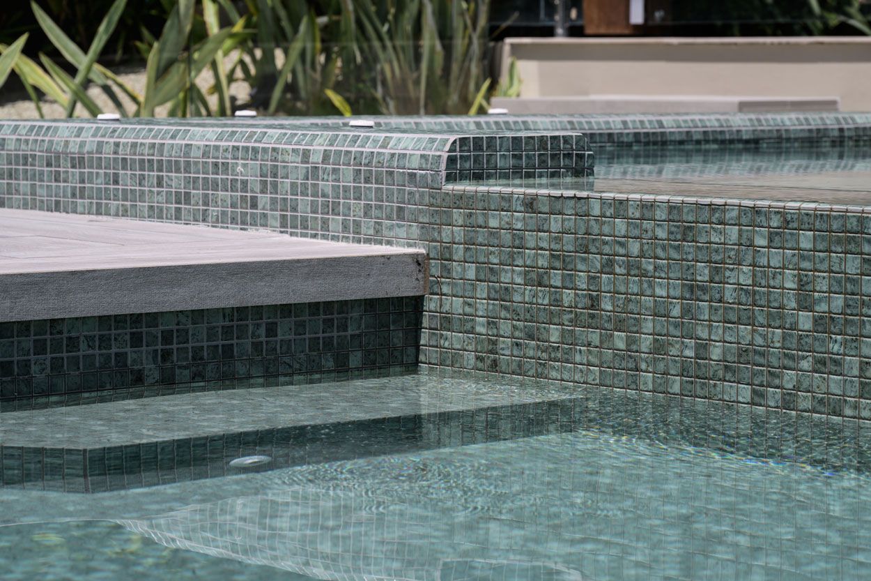 Performance Pool & Spa - tiled swimming pool with stepped ledge and clear blue water beside a stone deck