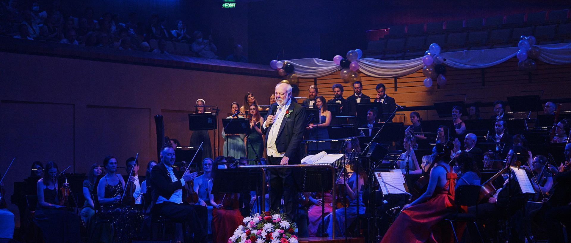 Queensland Pops Orchestra - Musician performing on stage with a band, blue-lit concert hall and audience in the foreground
