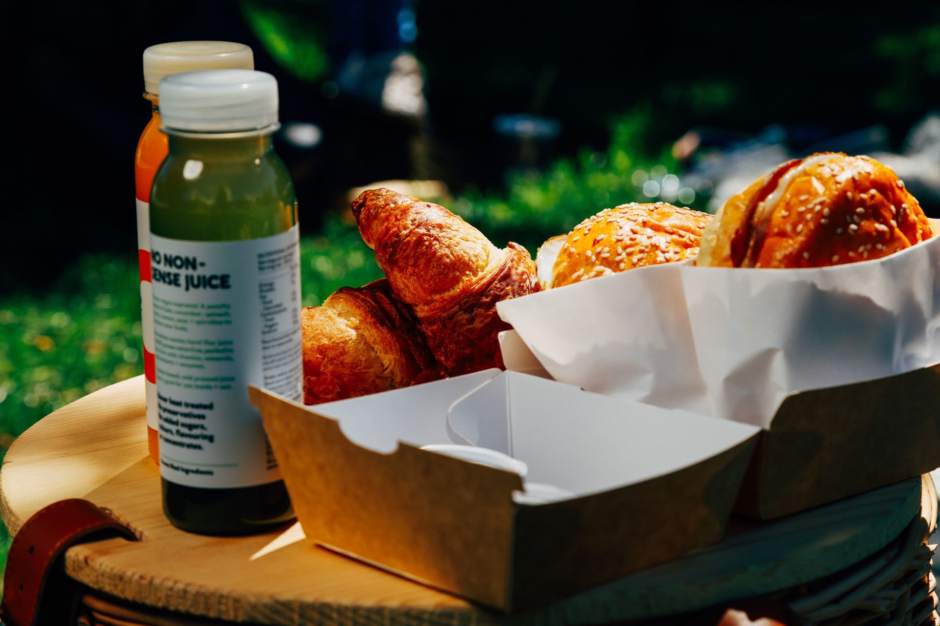 A basket of food and a bottle of juice on a table.