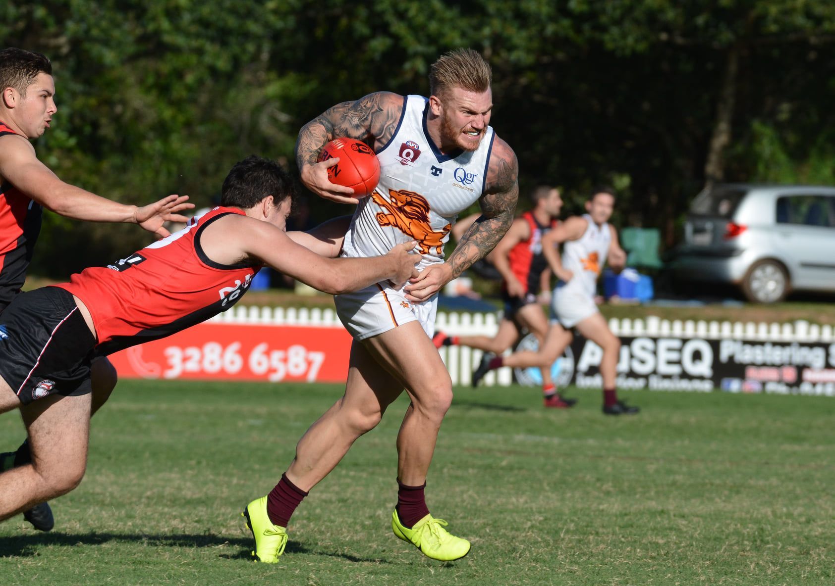 AFL Queensland - Australian rules football player being tackled while running with the ball on a grassy field