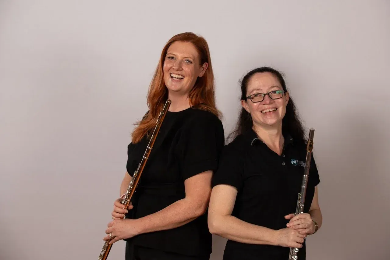 Brisbane Symphony Orchestra - Two musicians in black shirts holding woodwind instruments, standing back-to-back and smiling against a plain background