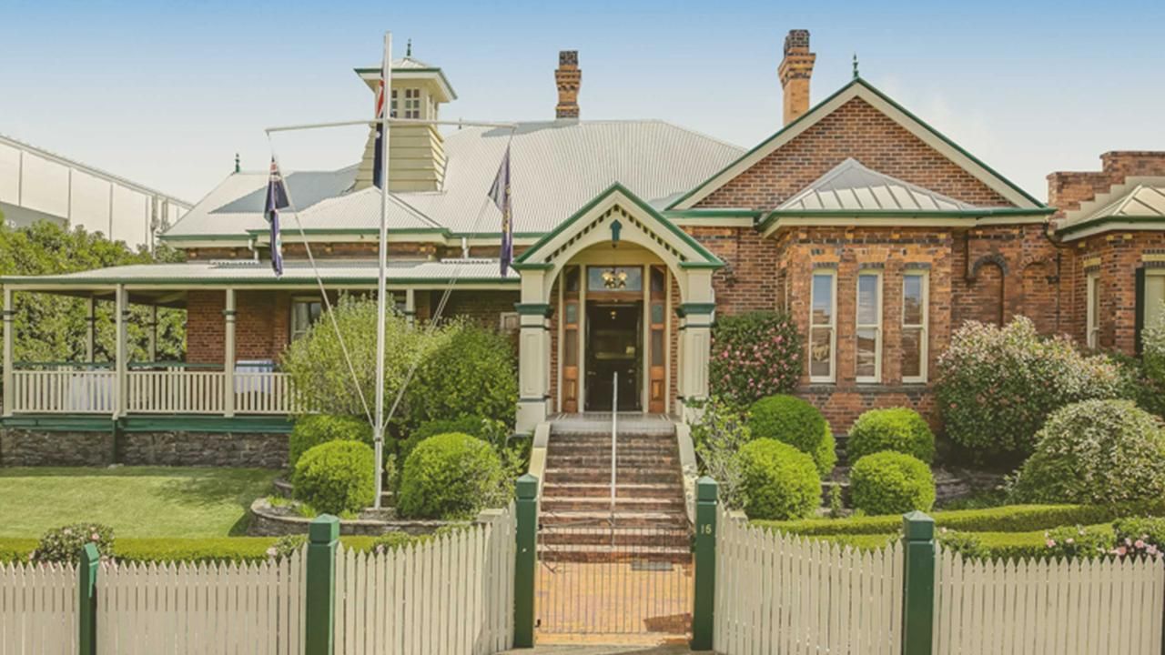 Downs Club - Front view of a brick Victorian house with a white picket fence, steps, and a manicured front garden