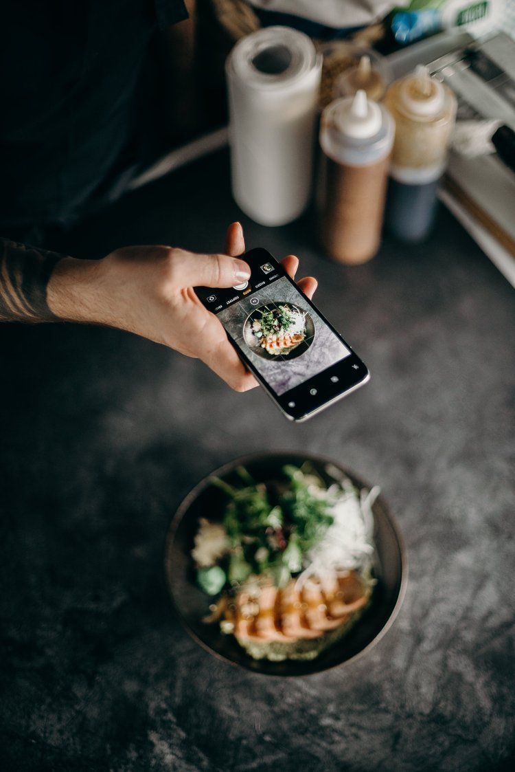 A person is taking a picture of a bowl of food with a cell phone.