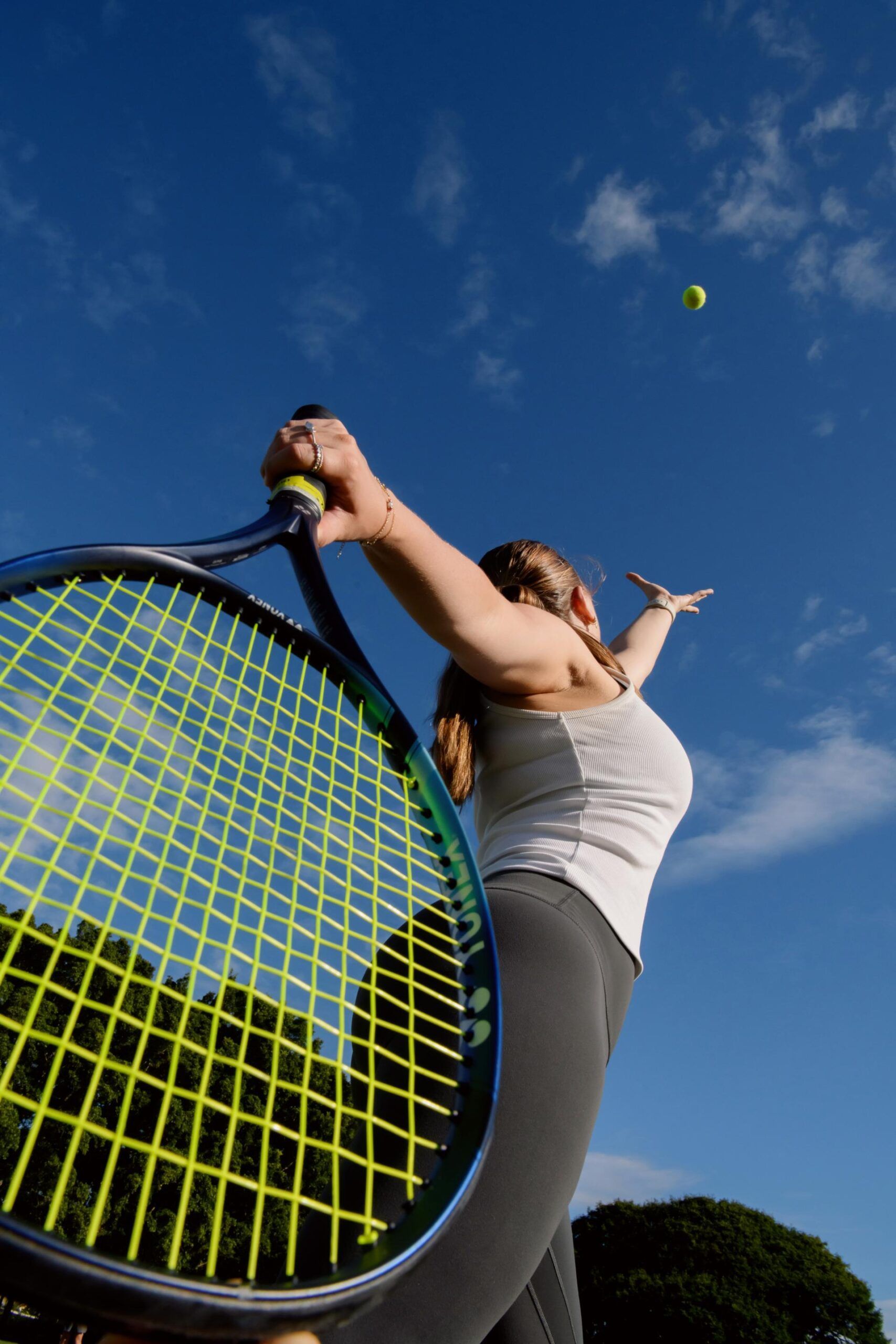 Bell Orthopaedics - Tennis player swings a racket on a court under a blue sky, with a ball in midair.