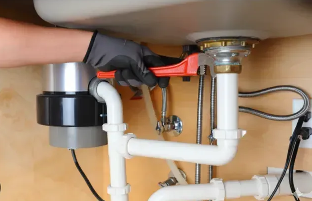 Person using a wrench to work on plumbing under a sink with a garbage disposal unit.