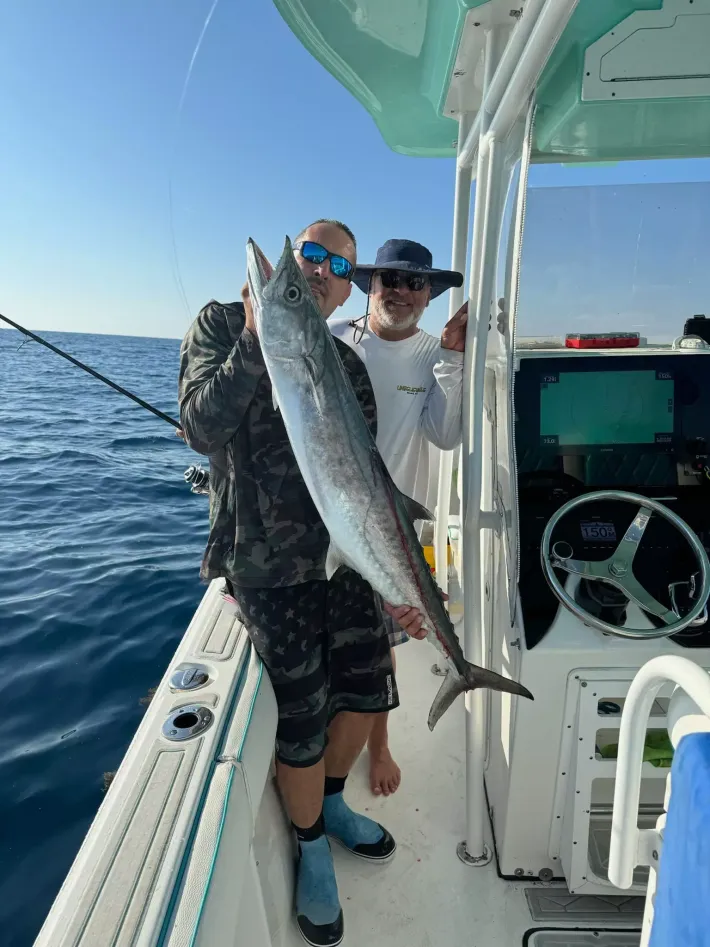 Two people on a boat hold up a large fish on a sunny day at sea.