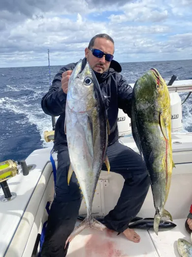 Angler on a boat holding two large fish on a cloudy open sea