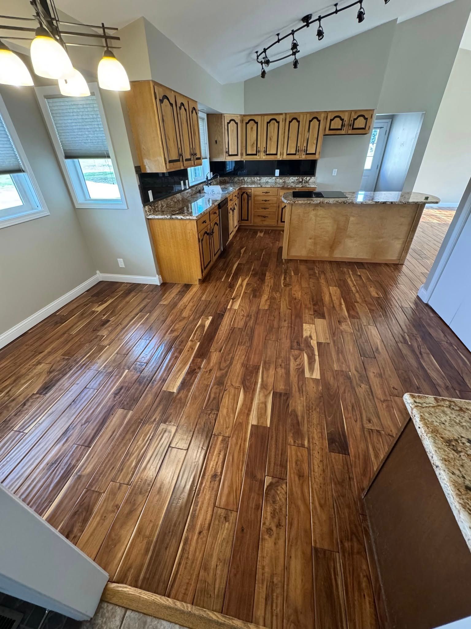 Hardwood floor in a kitchen with wooden cabinets and island, granite countertops, and light fixtures.