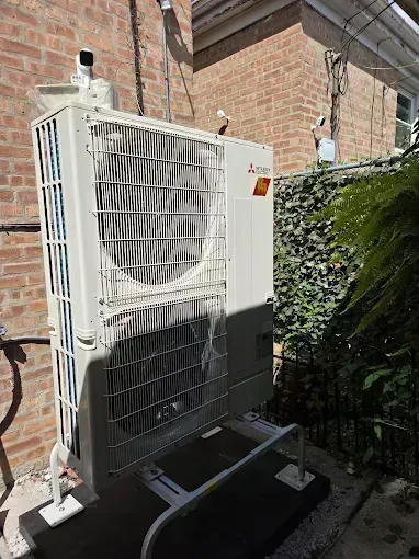 Mitsubishi air conditioner unit outside against brick wall, with protective metal cage.