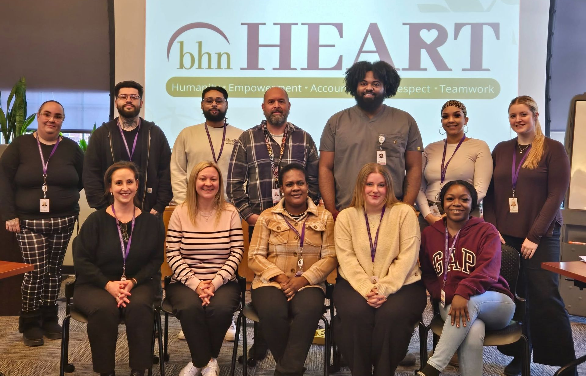 Staff who completed new employee orientation sitting together in front of a slide that shows our BHN HEART values statement (Humanity, Empowerment, Accountability, Respect & Teamwork)