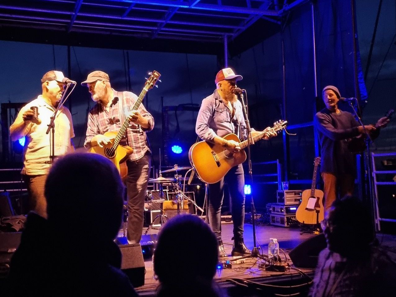en gruppe mænd står på scenen og spiller guitar og synger i mikrofoner