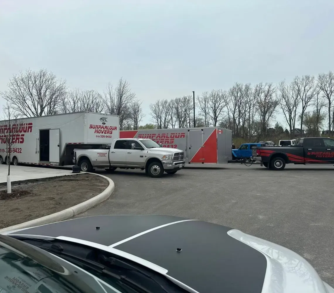 Two large trailers and two pickup trucks are parked on a paved lot on an overcast day.