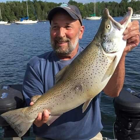 A man is holding a large fish in front of a body of water.