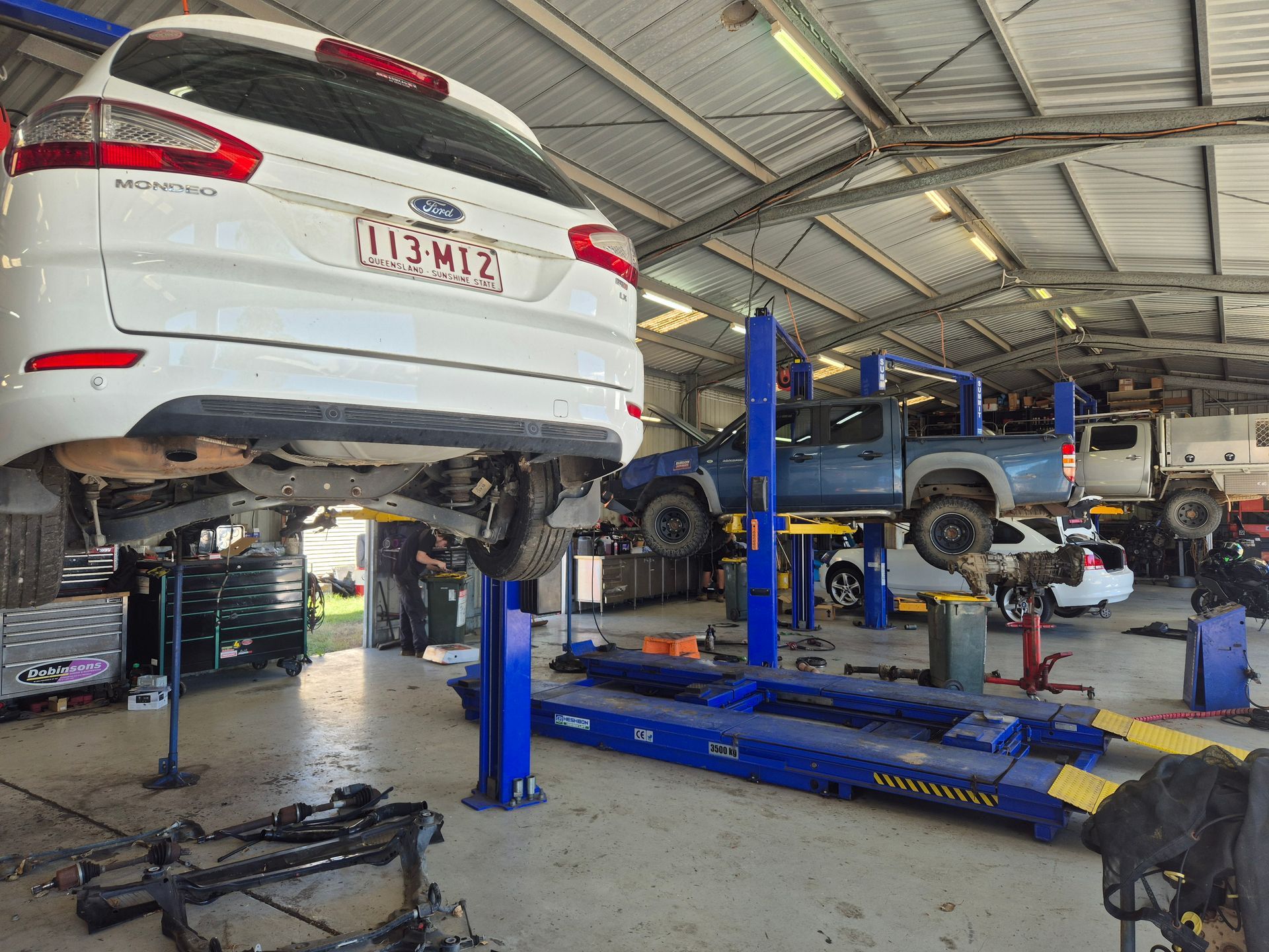 White SUV on a Lift in an Auto Repair Shop With Another Vehicle — Emu Park Automotive and Tyre Service in Emu Park, QLD