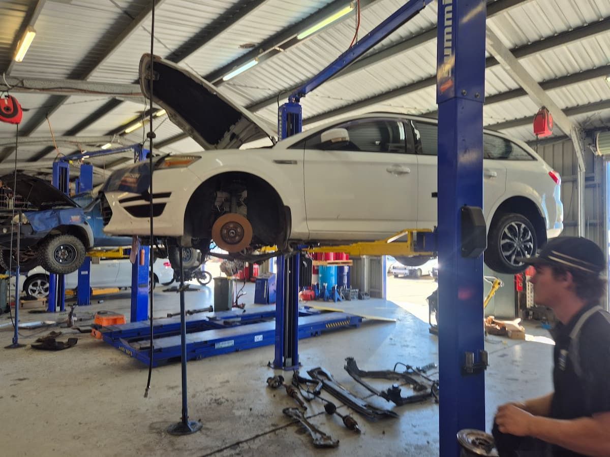 White Car on Lift in Auto Shop With Hood Open, Mechanic — Emu Park Automotive and Tyre Service in Taranganba, QLD