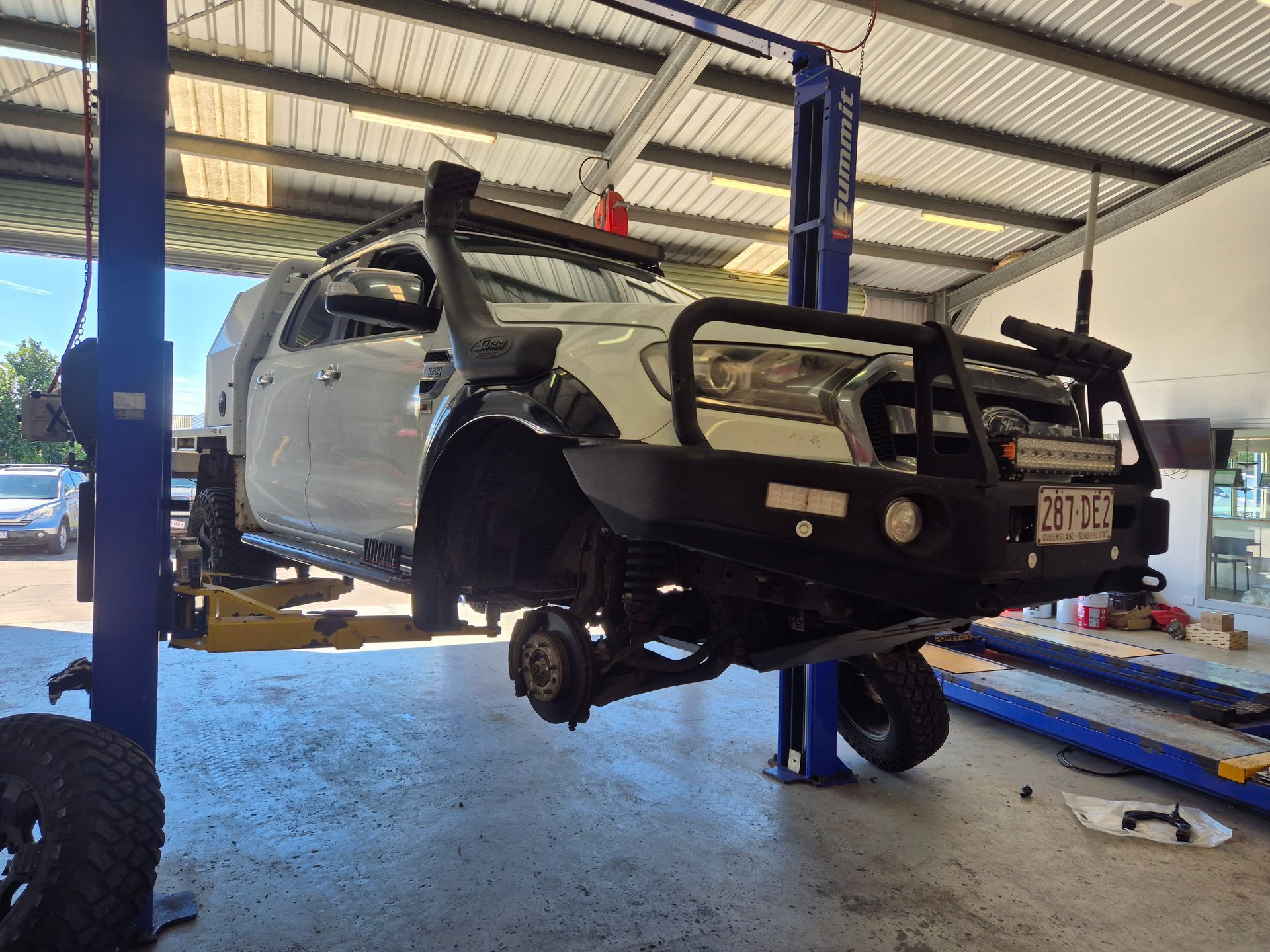 White off-road SUV lifted on a hydraulic hoist in an auto repair shop — Emu Park Automotive and Tyre Service in Emu Park, QLD