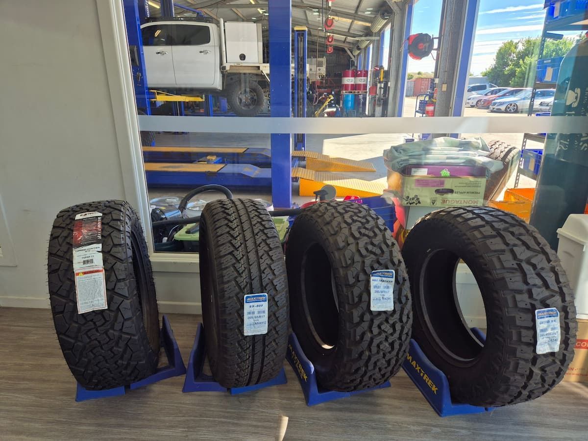 Four black off-road tires displayed on blue stands in a tire shop. — Emu Park Automotive and Tyre Service in Emu Park, QLD