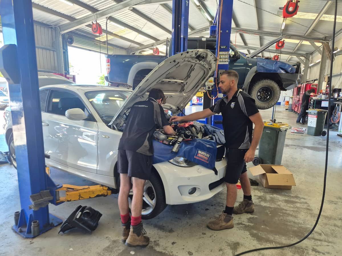 Two mechanics working on a white car in an auto repair shop, hood open on a lift. — Emu Park Automotive and Tyre Service in Emu Park, QLD