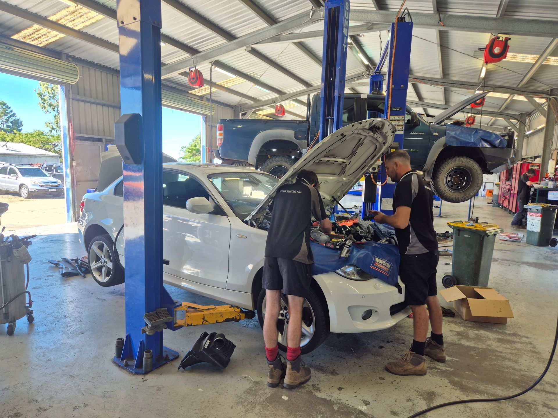 Two Mechanics Work on a White Car Lifted in an Auto Repair Shop — Emu Park Automotive and Tyre Service in Emu Park, QLD