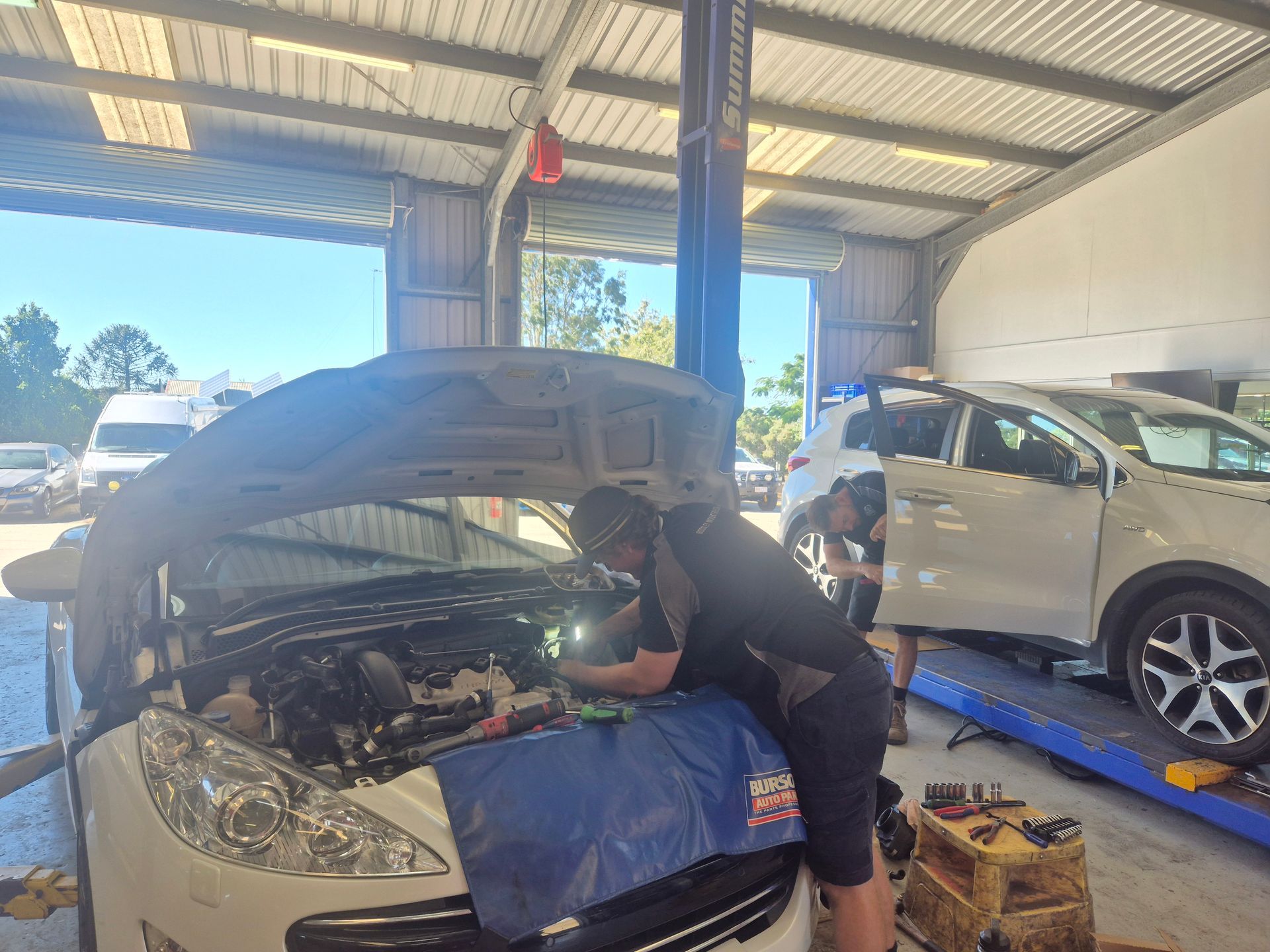 Mechanic Working Under Open Hood of a White Car in a Garage — Emu Park Automotive and Tyre Service in Emu Park, QLD