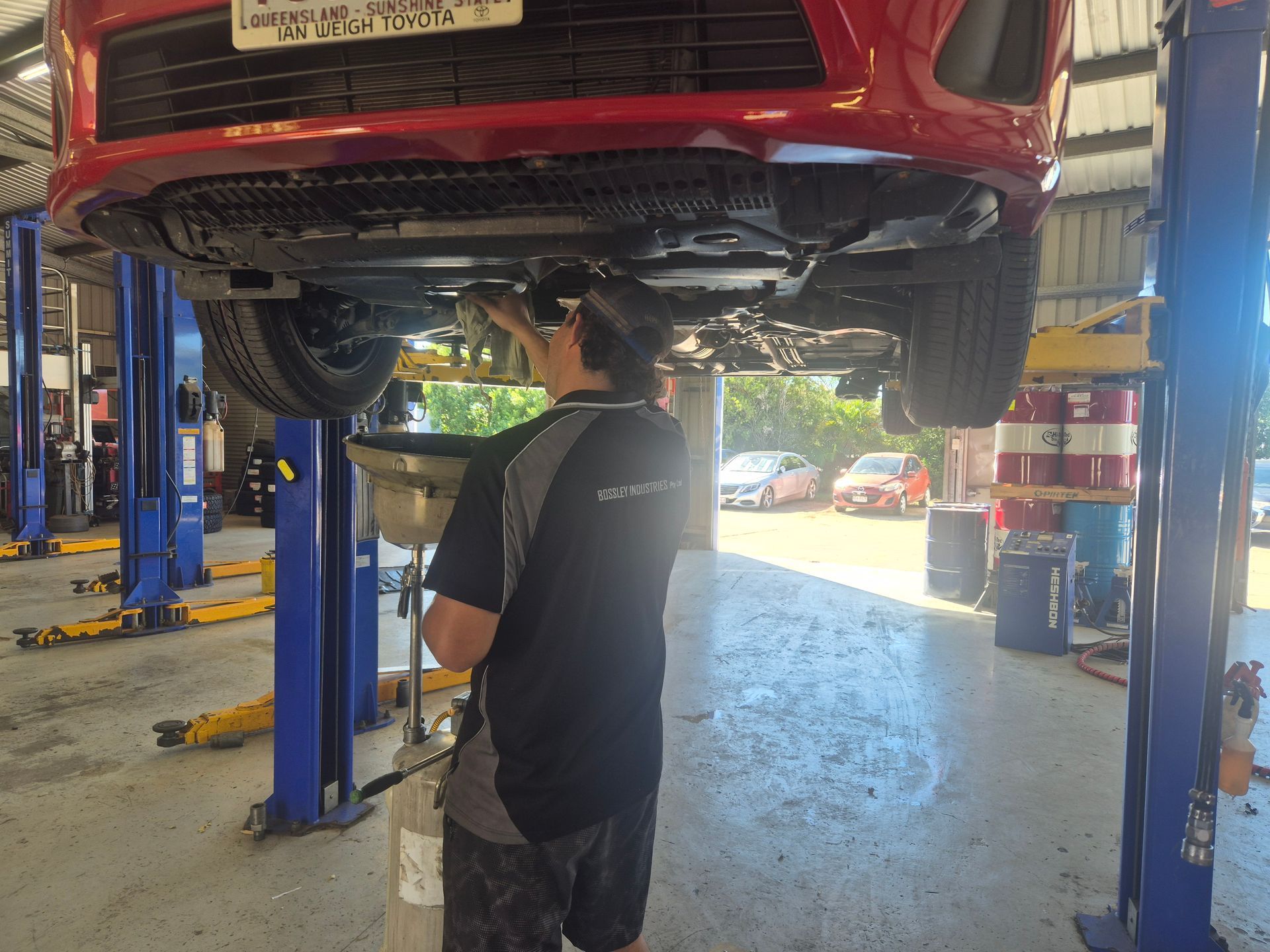 Mechanic working under a red car on a lift in an auto repair shop — Emu Park Automotive and Tyre Service in Emu Park, QLD