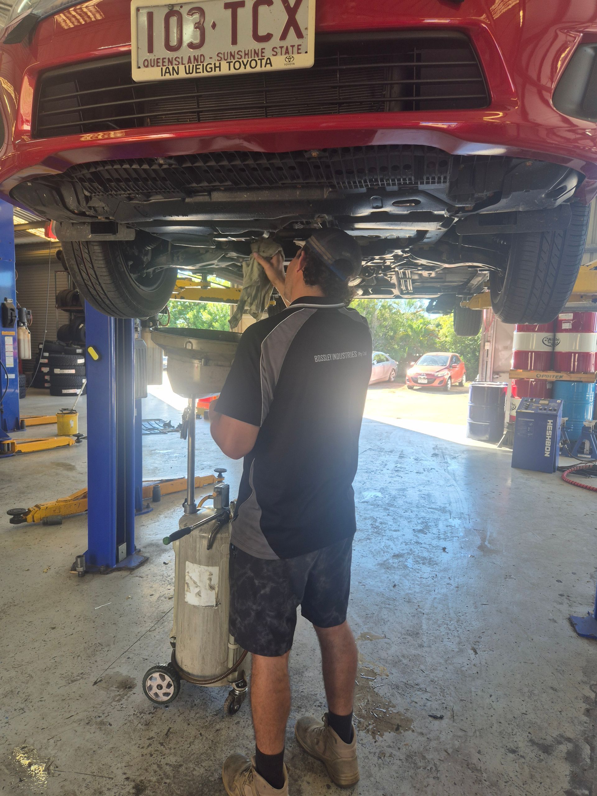 Mechanic Inspecting a Red Car on a Lift in an Auto Shop — Emu Park Automotive and Tyre Service in Emu Park, QLD