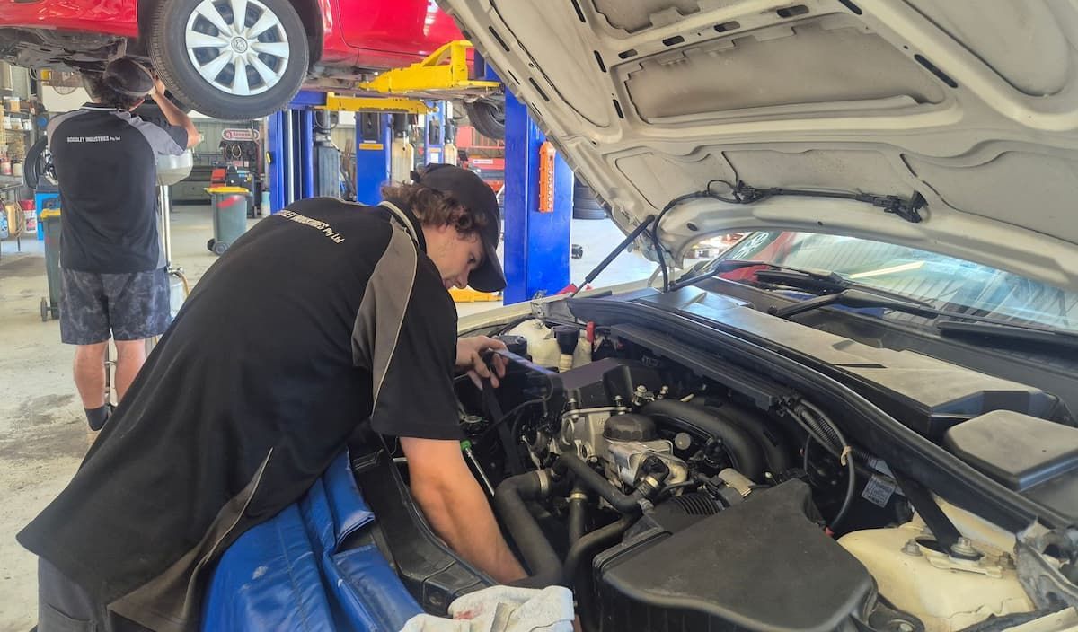 Mechanic inspecting a car engine in a repair shop while another vehicle is lifted nearby