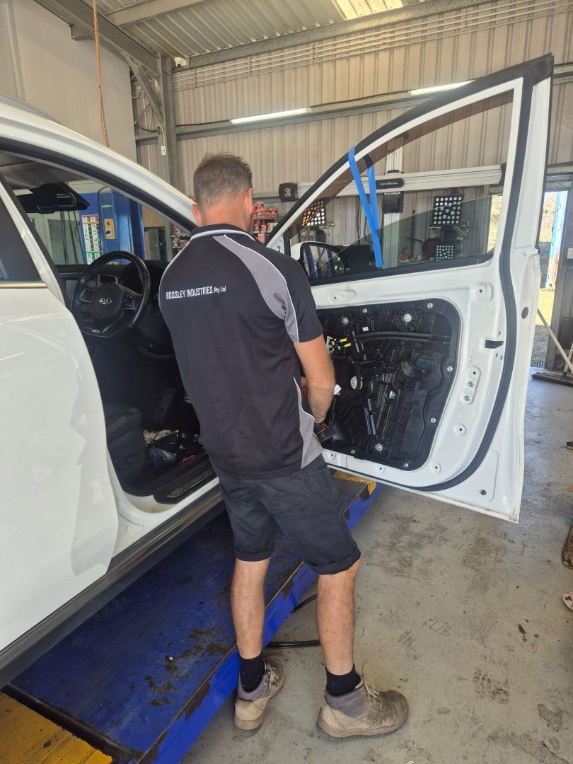 Mechanic inspecting a white car’s open door in a workshop, standing on a blue lift platform. — Emu Park Automotive and Tyre Service in Keppel Sands, QLD