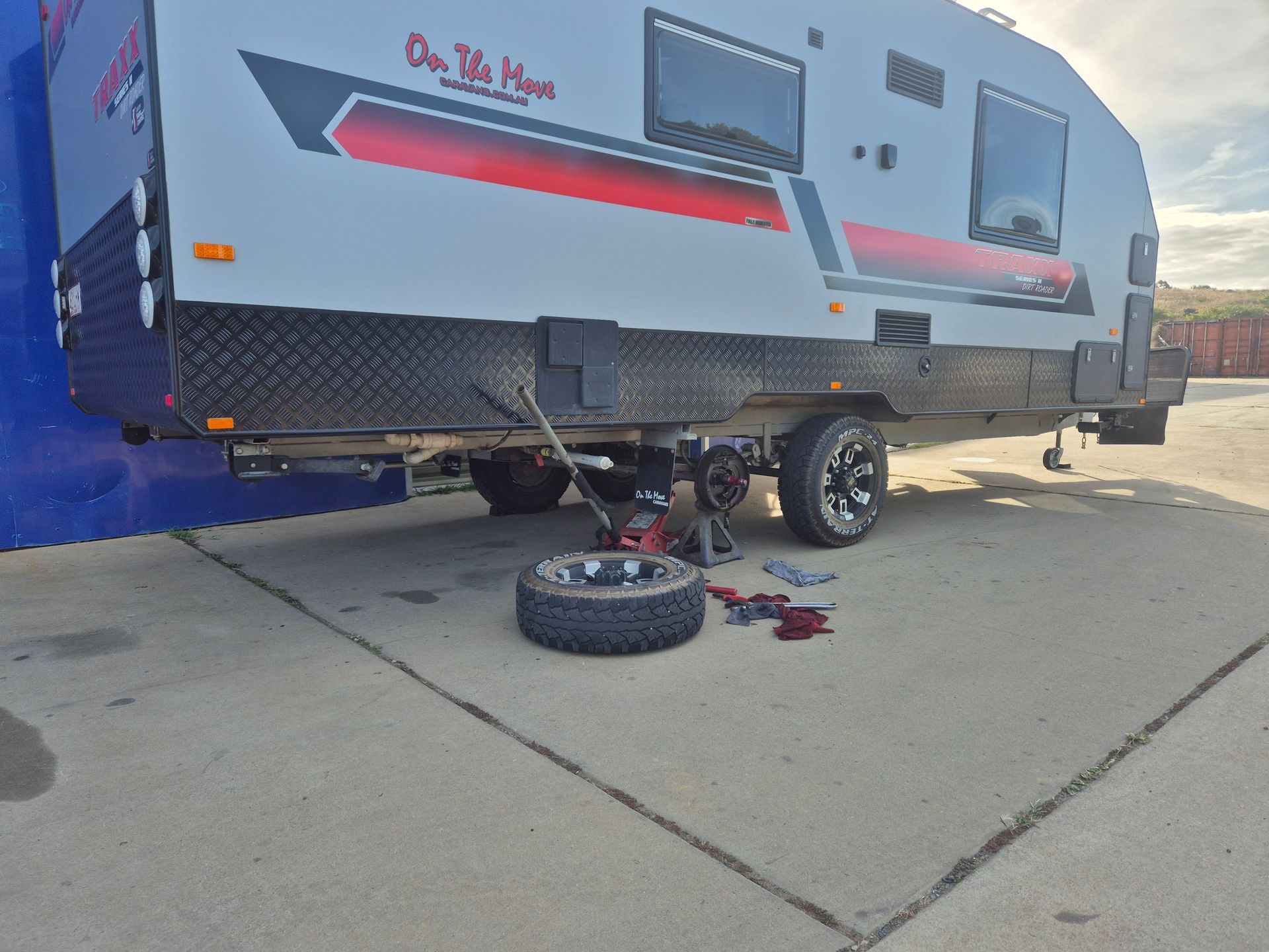 Camper trailer with a flat tire and tools on a concrete driveway, one wheel removed.— Emu Park Automotive and Tyre Service in Kinka Beach, QLD