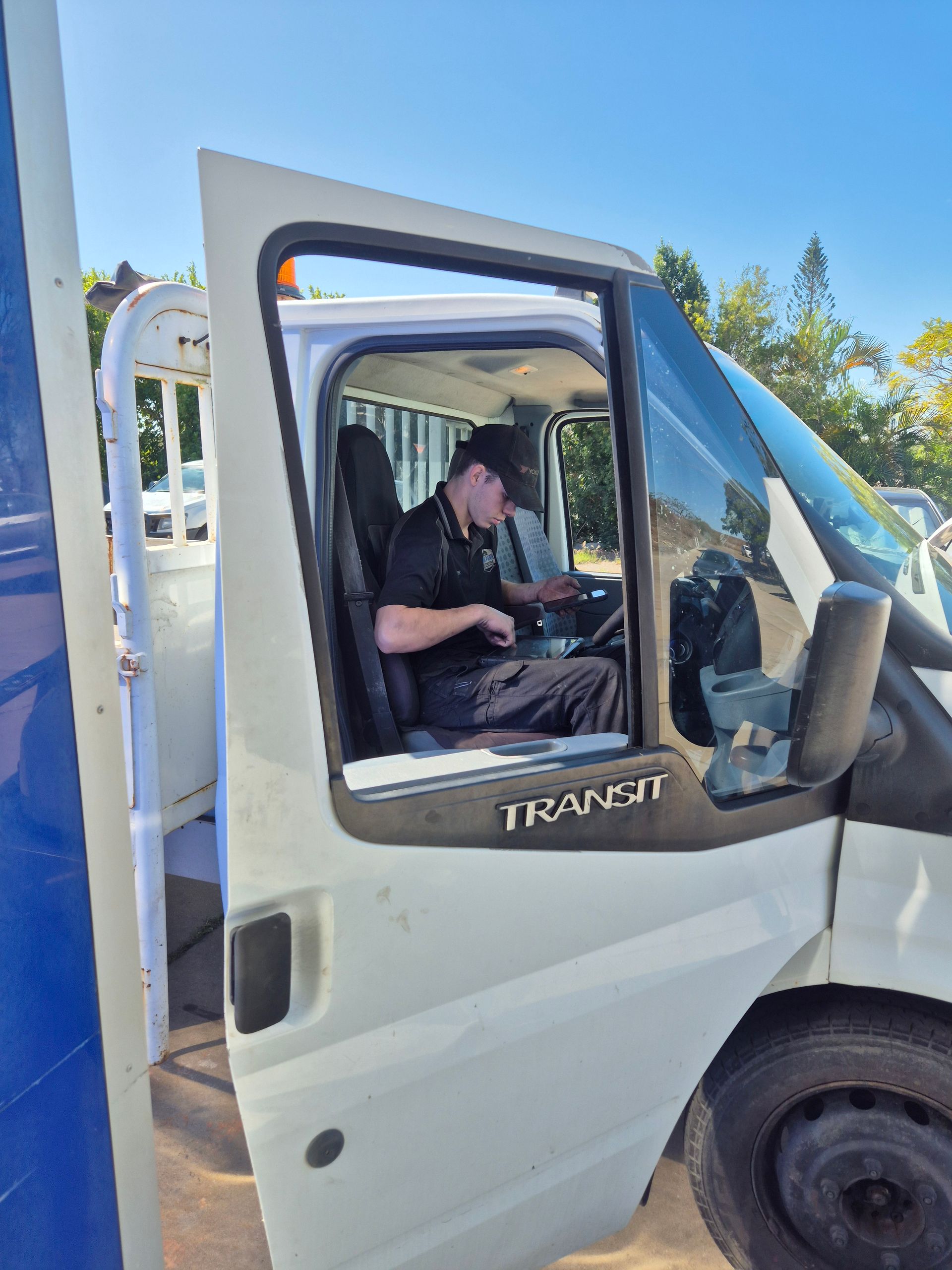 Driver seated in the cab of a white Transit van with the door open, outdoors in sunlight — Emu Park Automotive and Tyre Service in Emu Park, QLD