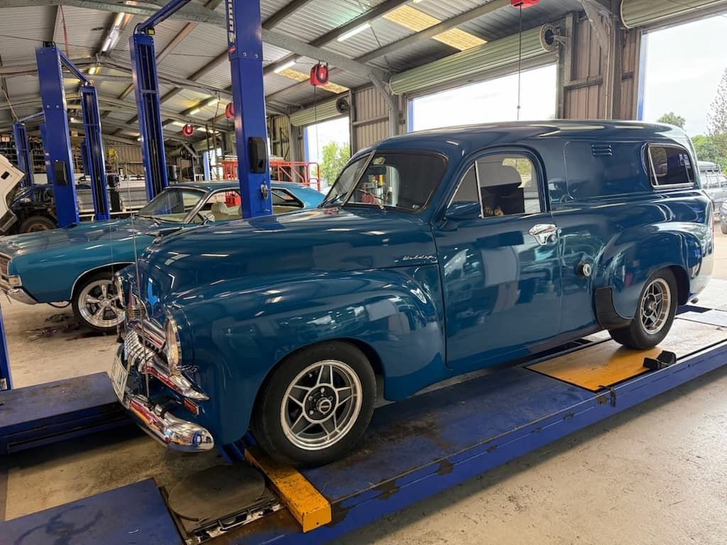 Blue vintage van on a lift in an auto workshop, with another classic car in the background. — Emu Park Automotive and Tyre Service in Kinka Beach, QLD