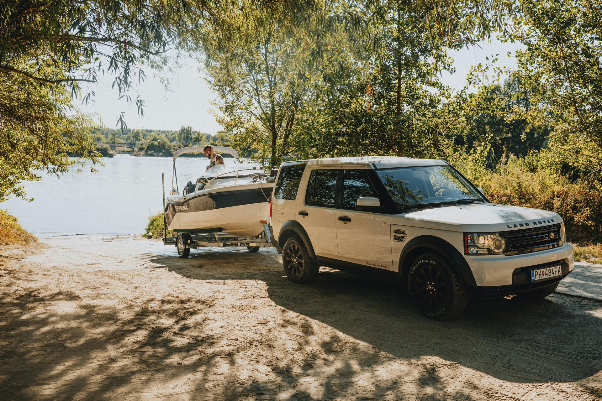 White SUV towing a boat trailer on a sandy lakeside road under trees — Emu Park Automotive and Tyre Service in Keppel Sands, QLD