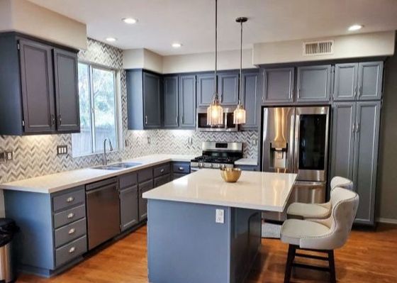 Modern kitchen with gray cabinets, white island, pendant lights, and stainless steel appliances.