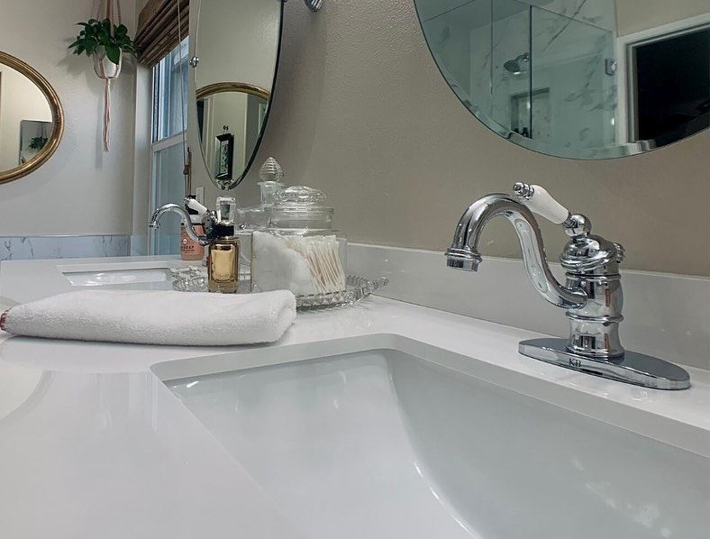 Bathroom sink with chrome faucet, mirror, folded towel, and toiletries on a white countertop.