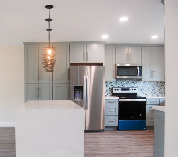 Modern kitchen with gray cabinets, stainless appliances, pendant light, and white island.