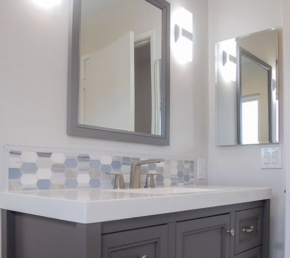 Modern bathroom vanity with white countertop, gray cabinets, mirror, and blue-gray tile backsplash
