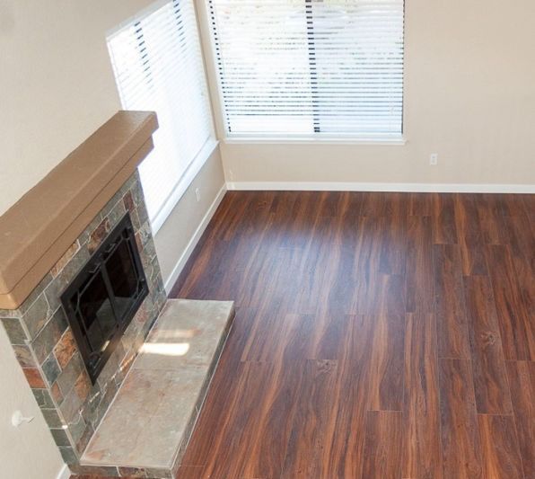 Empty living room with a fireplace, hardwood floors, and large windows with blinds.