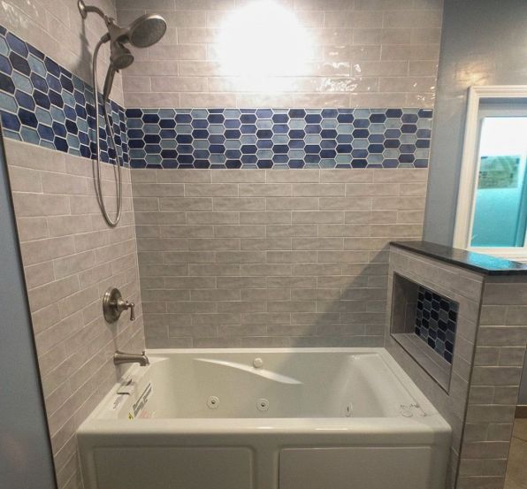 Bathroom with a white bathtub, gray tile walls, blue mosaic accent strip, and glass shower enclosure