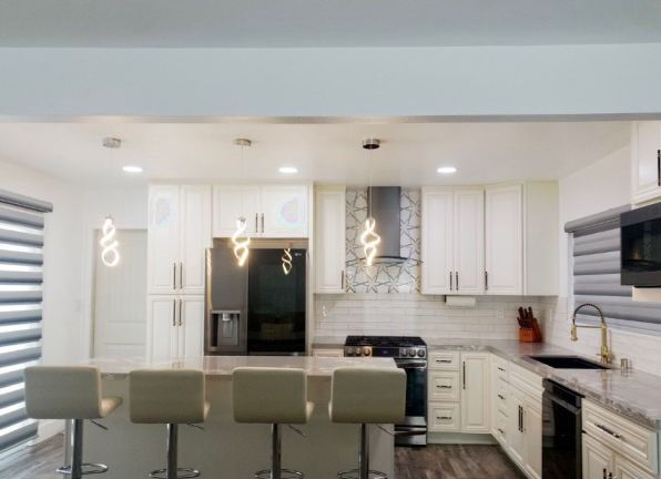 Modern white kitchen with island, pendant lights, bar stools, and stainless steel appliances