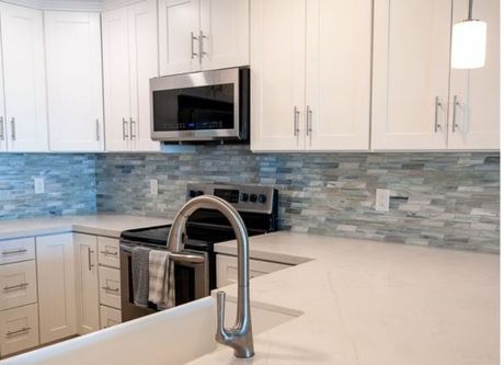 Modern white kitchen with stainless steel appliances, blue tile backsplash, and countertop sink faucet