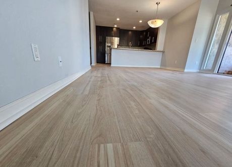 Empty open-plan living room with light wood flooring and a kitchen in the background