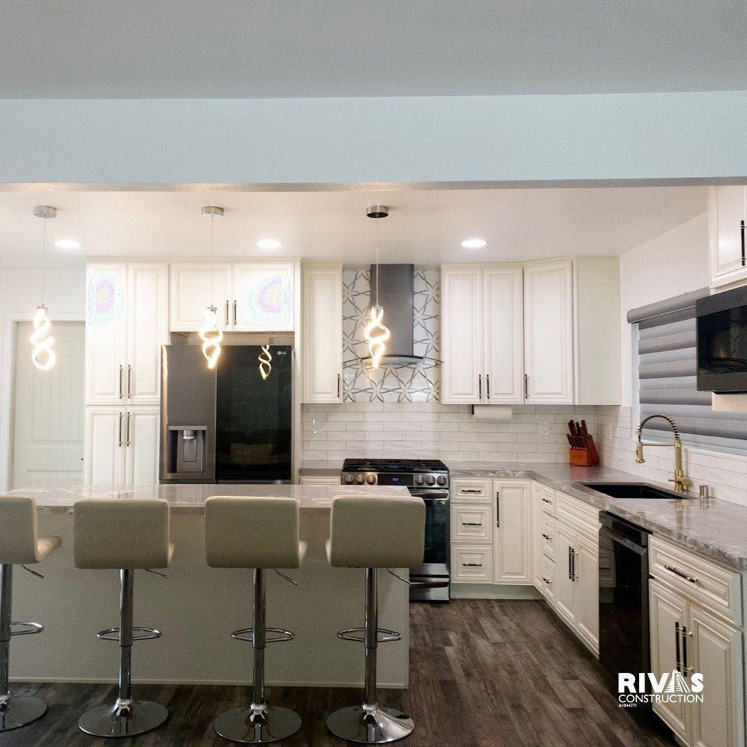 Modern white kitchen with island bar stools, pendant lights, stainless appliances, and gray tile floor